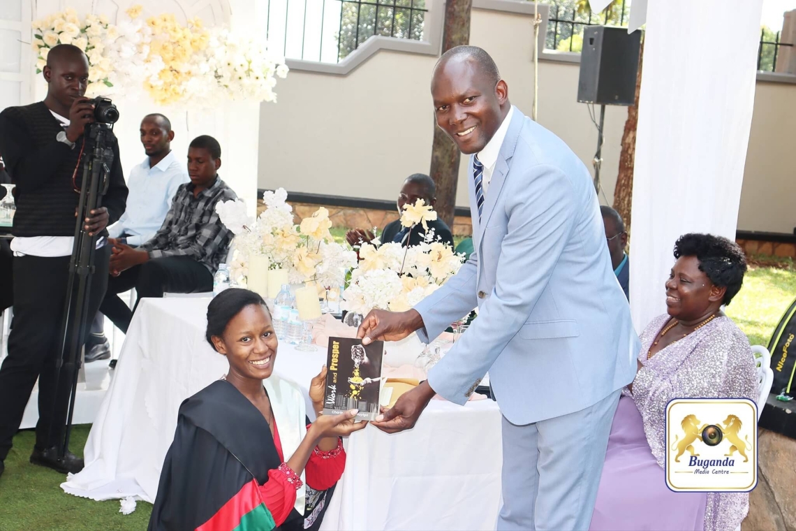Owek. Noah Kiyimba presents Cossy Baagala with Work and Prosper, a book by Katikkiro Charles Peter Mayiga, urging her to embrace its lessons Owek. Noah Kiyimba presents Cossy Baagala with Work and Prosper, a book by Katikkiro Charles Peter Mayiga, urging her to embrace its lessons